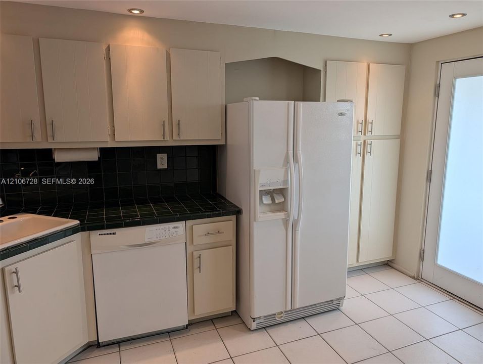 Kitchen featuring flat-panel cabinetry, tiled countertops, built-in dishwasher, side-by-side refrigerator, and tile flooring