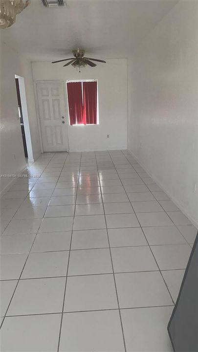 Interior space featuring white floor tiles, a six-panel exterior door, and a ceiling-mounted fan