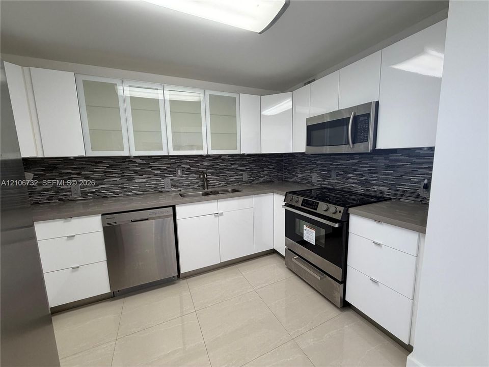 Kitchen featuring high-gloss white cabinetry, frosted glass cabinet doors, stone-finish countertops, stainless steel appliances, and a linear tiled backsplash
