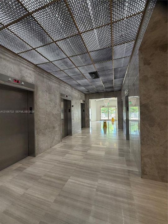 Lobby featuring stone wall cladding, polished stone flooring, grid-pattern ceiling detailing, and stainless steel elevator doors