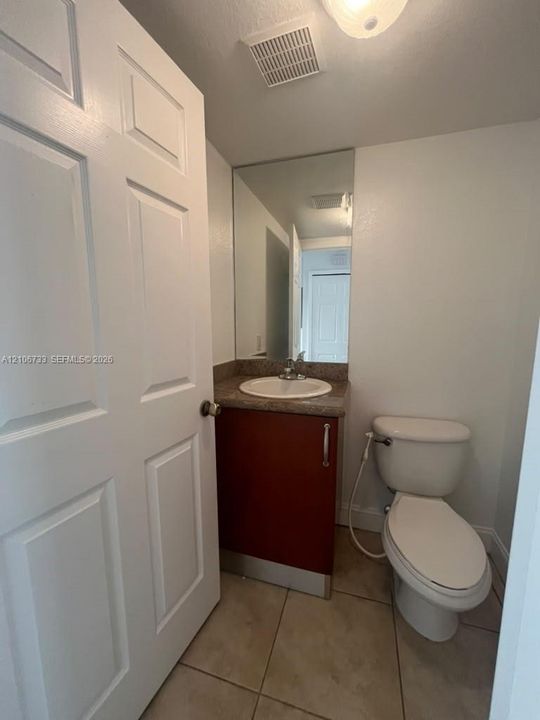 Half Bathroom featuring a vanity with a stone-finish countertop, integrated sink, vertical mirror, and ceramic tile flooring