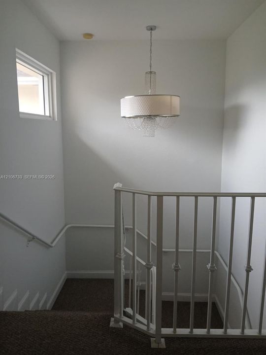 Drum-style pendant chandelier with crystal accents, white metal railing, and high-reaching ceiling