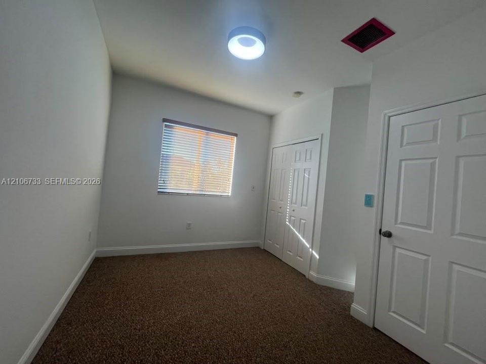 Room featuring neutral wall tones, carpeted flooring, a flush-mount circular light fixture, and double-panel closet doors