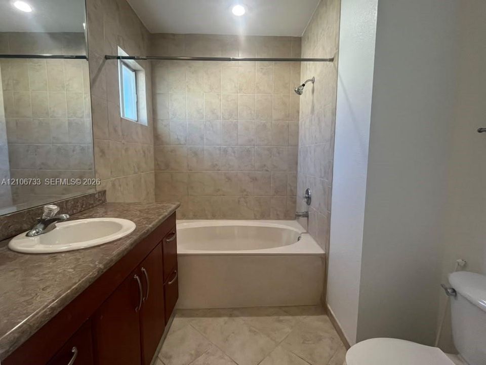 Bathroom featuring a wood-finish vanity with a stone-composite countertop, integrated sink, porcelain tile flooring, and a tiled shower surround with a soaking tub