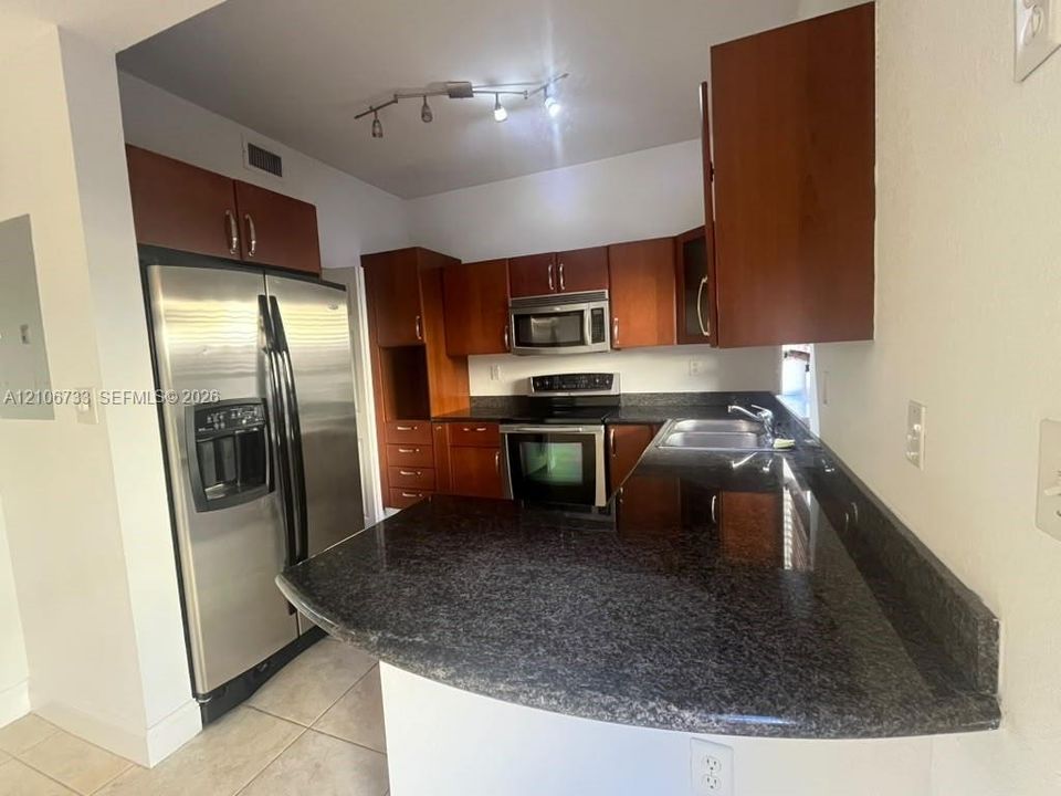 Kitchen featuring wood cabinetry, dark stone countertops, stainless steel side-by-side refrigerator, built-in microwave, and track lighting