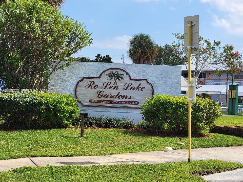 Community entrance sign featuring textured masonry walls, manicured landscaping, and mature palm trees