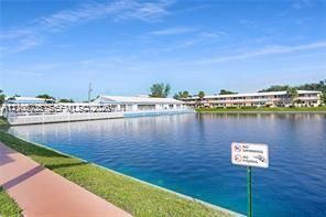 Waterfront setting featuring a tiered multi-story building, an expansive paved promenade, and a manicured grassy perimeter