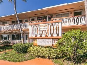 Mid-century exterior featuring decorative latticed balcony railings, clean stucco facade, and established tropical landscaping