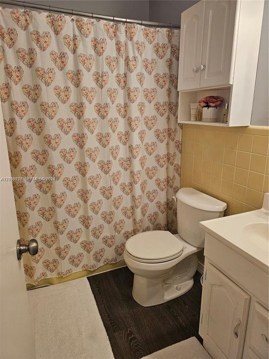 Bathroom featuring wood-finish flooring, square ceramic wall tiling, white vanity cabinet with integrated sink, and white wall-mounted storage cabinetry