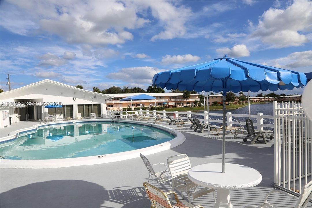 Outdoor swimming pool featuring concrete decking and white vinyl perimeter fencing, situated alongside a water feature