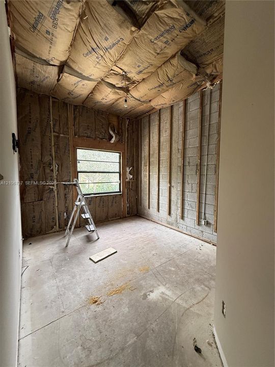Interior space featuring concrete block construction, exposed wall framing, fiberglass batt insulation, and a single-pane window