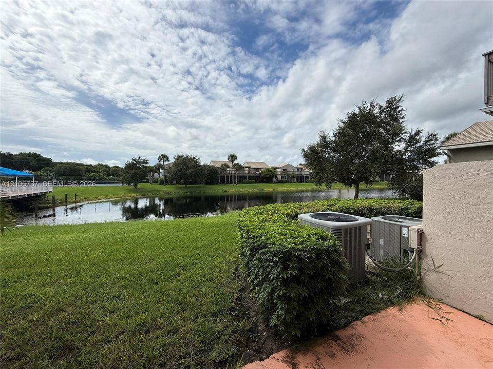 Waterfront property featuring a pond, manicured lawn, hedge landscaping, and exterior HVAC units