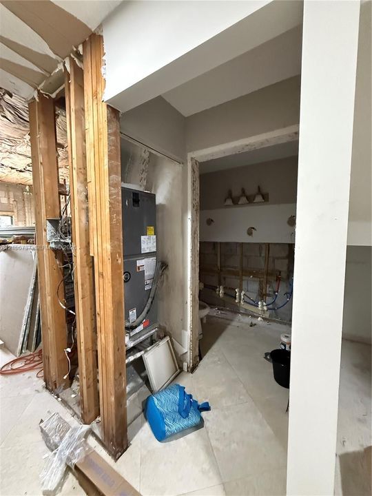 Interior space featuring exposed wood framing, a vertical HVAC unit, large-format tile flooring, and exposed wall plumbing