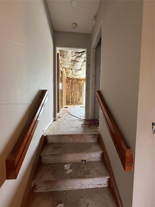 Stairway featuring wood-finish handrails on both sides, leading to an interior space with exposed wall studs and unfinished insulation
