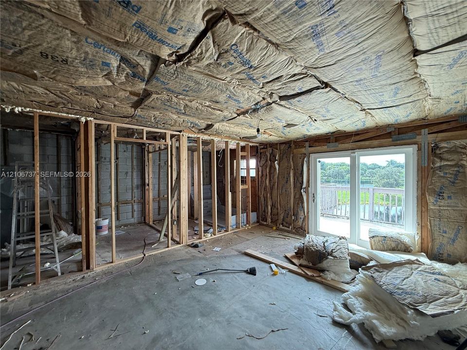 Unfinished interior space featuring exposed wood framing, concrete flooring, and double-glass sliding doors opening to an exterior deck