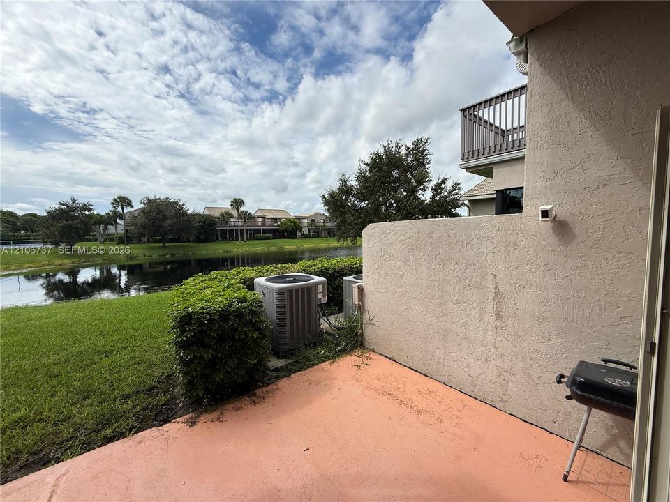 Concrete patio featuring a stucco privacy wall, second-story balcony with railings, and water frontage
