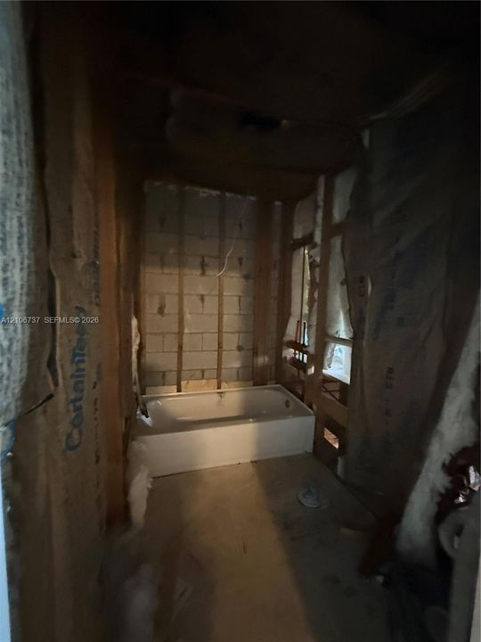 White rectangular bathtub set within an unfinished space featuring exposed concrete block walls, wood stud framing, and fiberglass insulation