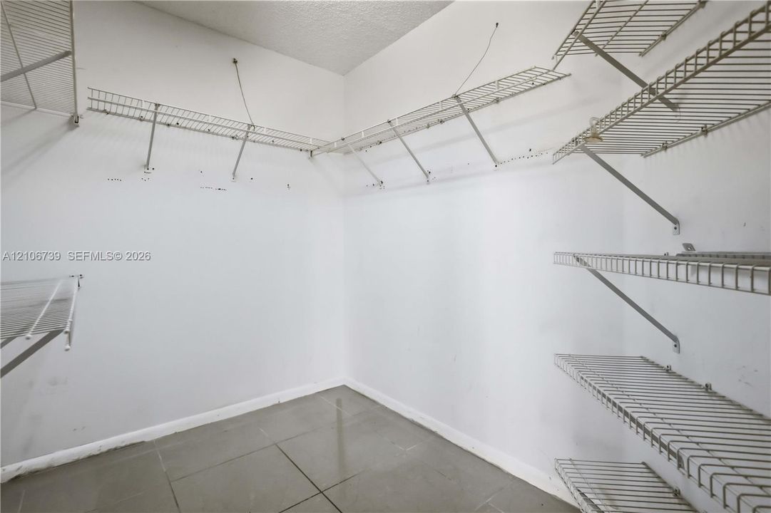 Storage space featuring white walls, neutral large-format floor tiles, and multi-tiered wall-mounted metal wire shelving