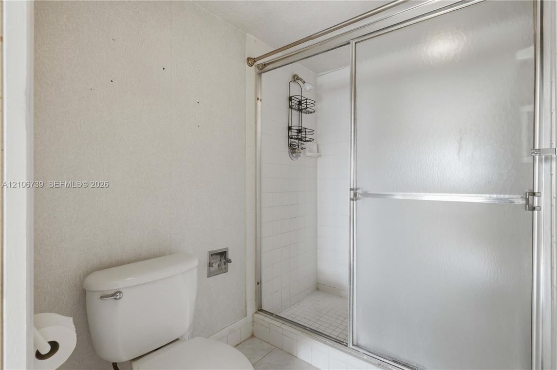 Full bathroom featuring a glass-enclosed shower stall with tiled interior, white toilet, and tile flooring