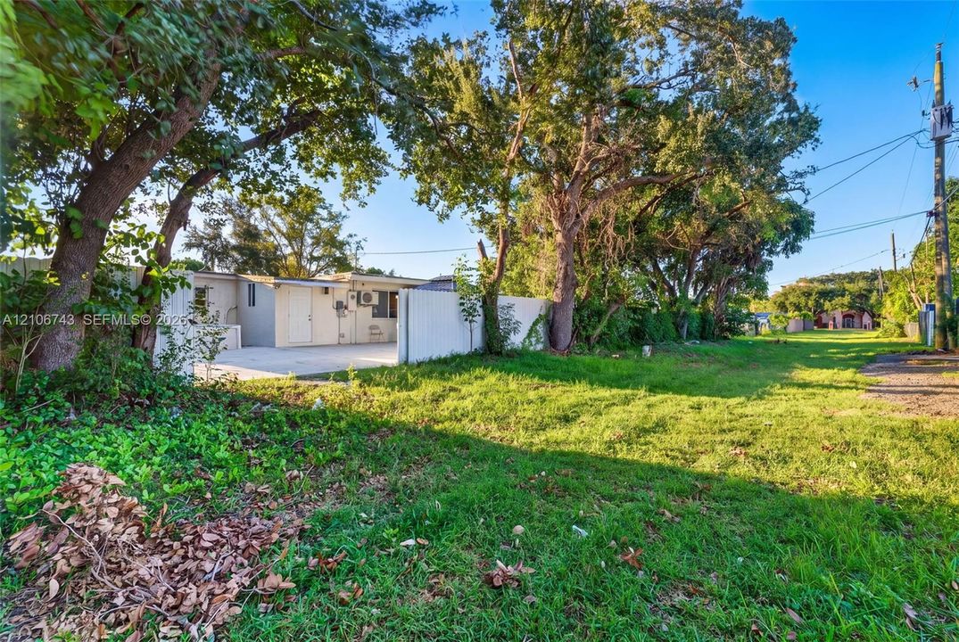 Exterior lot featuring a grass lawn, mature trees, and a white privacy fence