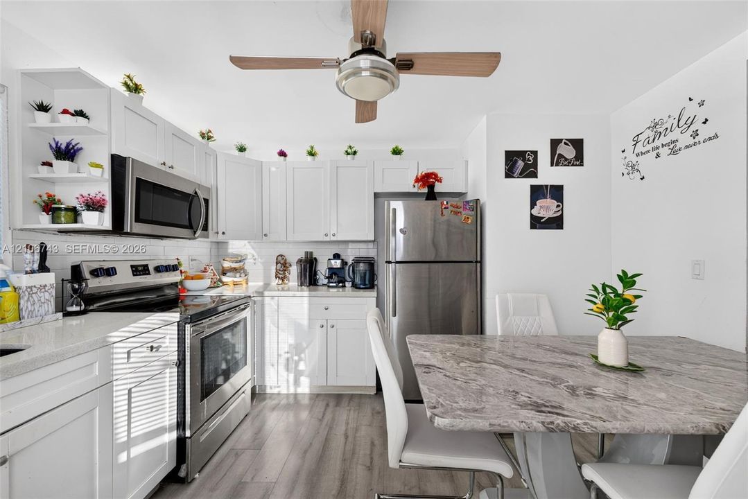 Kitchen featuring white Shaker-style cabinetry, stainless steel appliances, light-toned stone-patterned countertops, wood-finish flooring, and a ceiling-mounted light and fan fixture