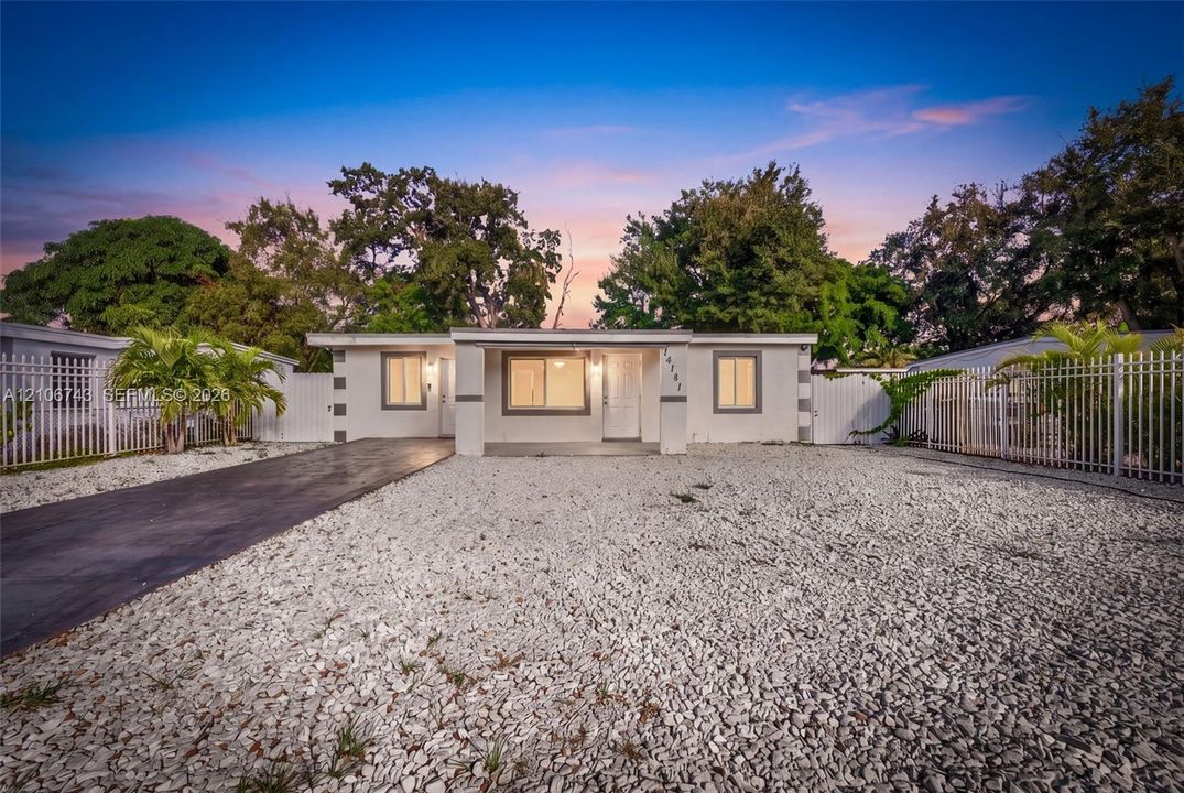Single-story residence featuring a paved driveway, light-toned exterior finish, white metal perimeter fencing, and decorative stone landscaping