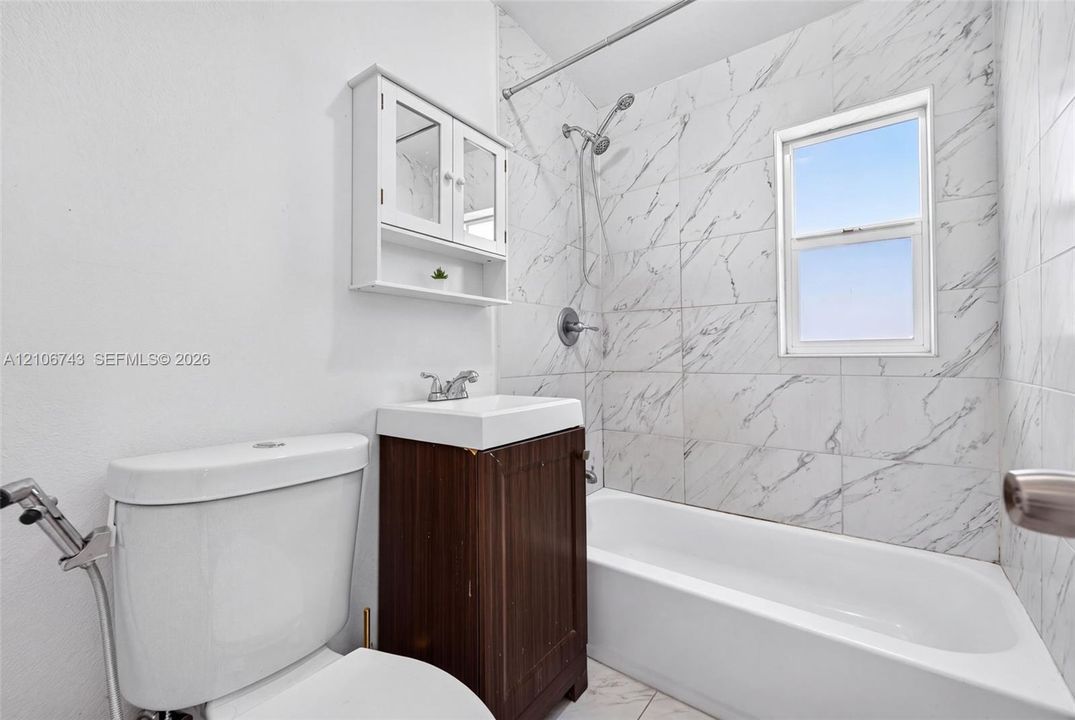 Bathroom featuring a tub and shower combination with full-height stone-finish wall tile, a wood-finish vanity with an integrated sink, and a wall-mounted medicine cabinet