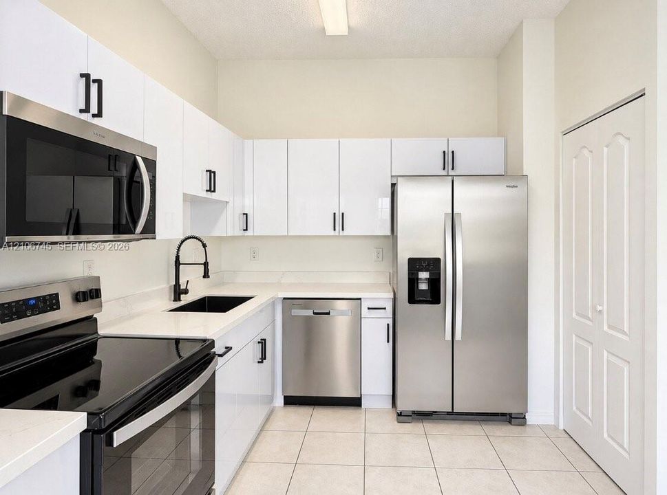 Kitchen featuring white flat-panel cabinetry, light-toned stone countertops, black hardware, stainless steel appliances, and tile flooring