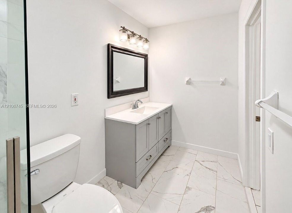 Bathroom featuring a gray vanity with an integrated countertop and basin, large-format tile flooring, a framed wall mirror, and a glass-enclosed shower