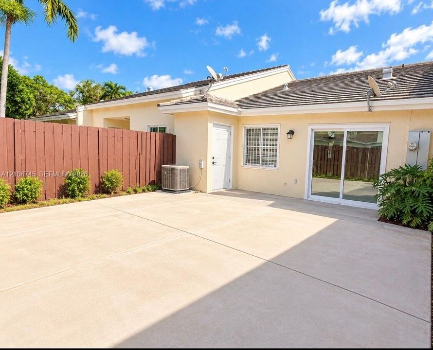 Stucco exterior featuring a concrete patio, tall perimeter wood fencing, sliding glass doors, and a tiled roof