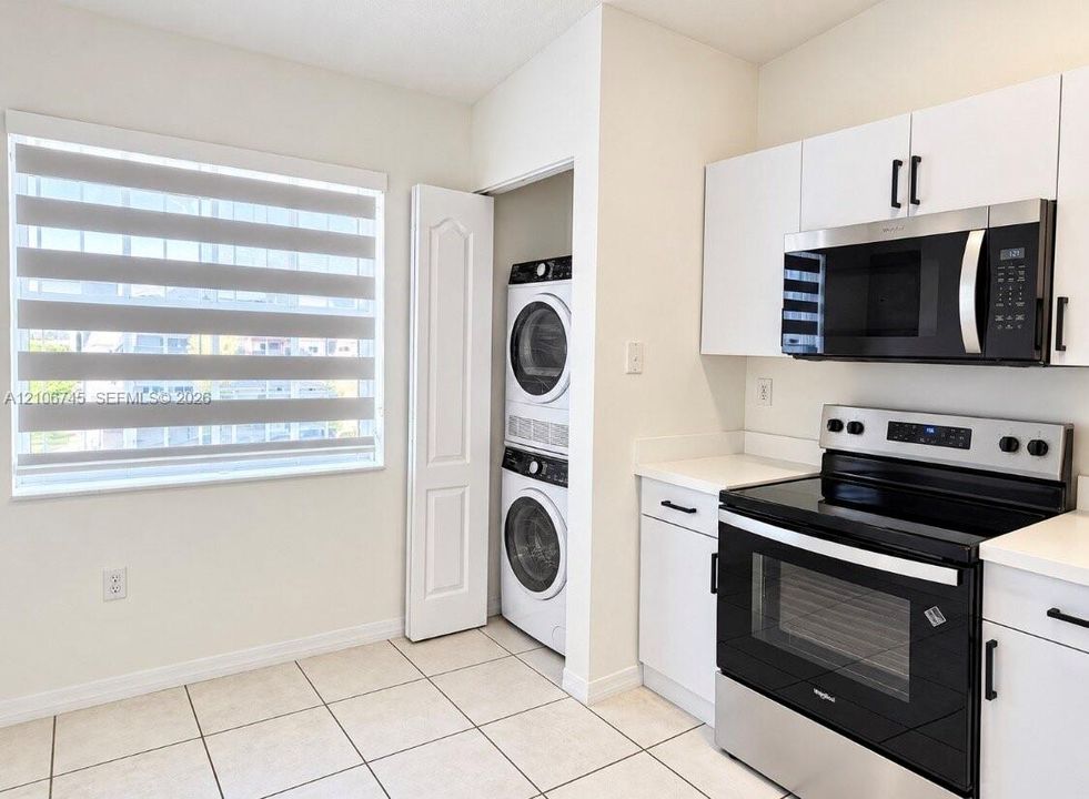Kitchen featuring white cabinetry, stainless steel appliances, a built-in laundry closet with stacked washer and dryer units, and light-toned tile flooring