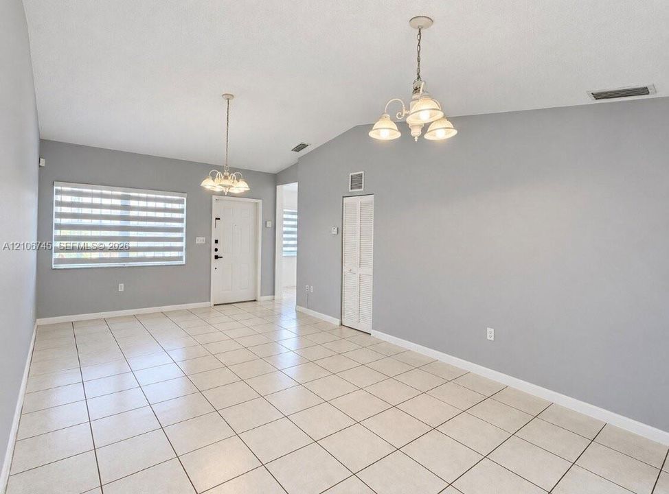 Open interior featuring high vaulted ceilings, large-format tile flooring, dual multi-arm chandeliers, and crisp neutral wall tones