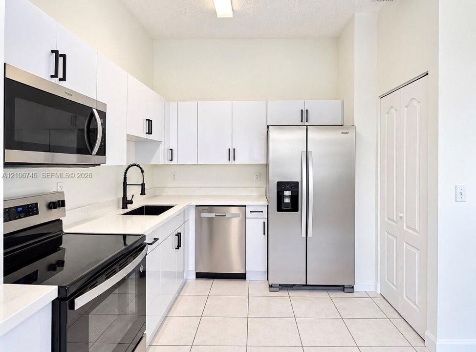 Kitchen featuring white cabinetry, quartz countertops, stainless steel appliances, a black faucet with undermount sink, and tiled flooring
