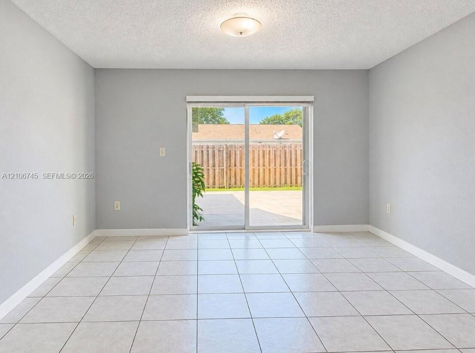 Neutral-toned interior featuring large-format ceramic tile flooring, sliding glass patio door, and flush-mount ceiling lighting