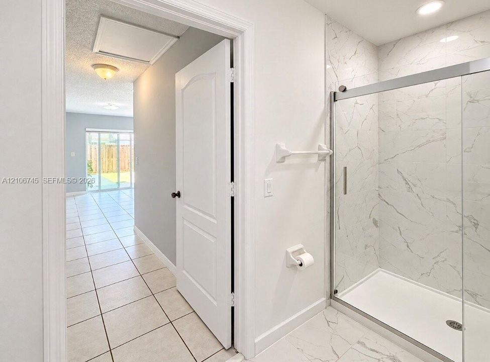 Bathroom featuring a walk-in shower with stone-patterned tile surround, glass sliding enclosure, and light-toned ceramic floor tiling