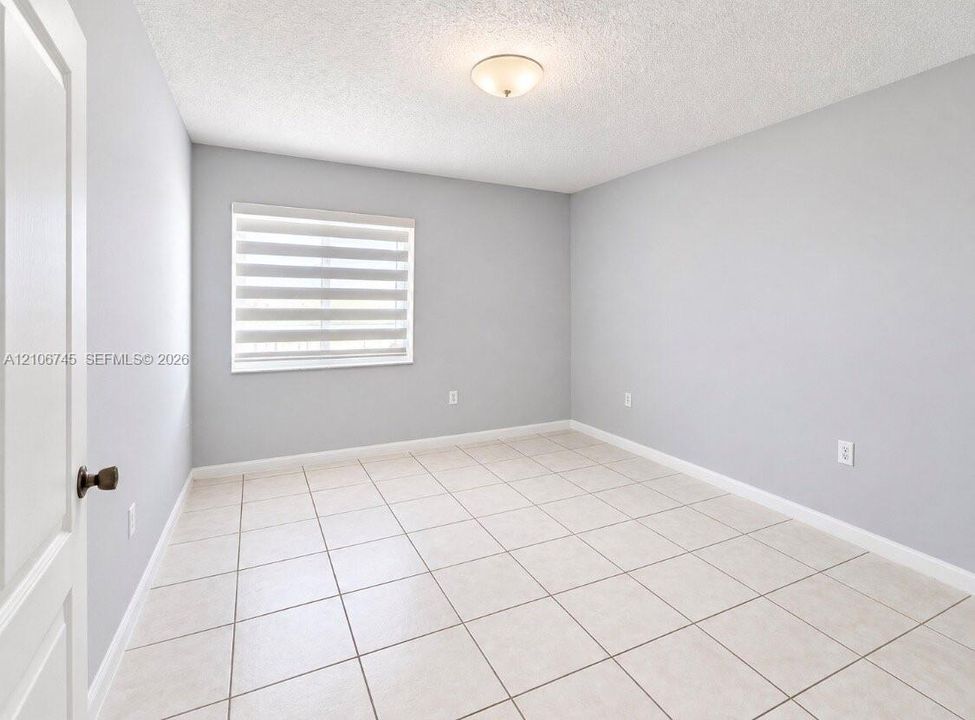 Neutral-toned interior space featuring tile flooring, a window with installed roller shades, and a ceiling-mounted dome light fixture