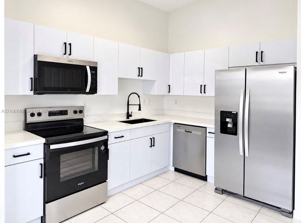 Kitchen featuring white flat-panel cabinetry, stainless steel appliances, solid surface countertops, a matte black high-arch faucet, and tile flooring