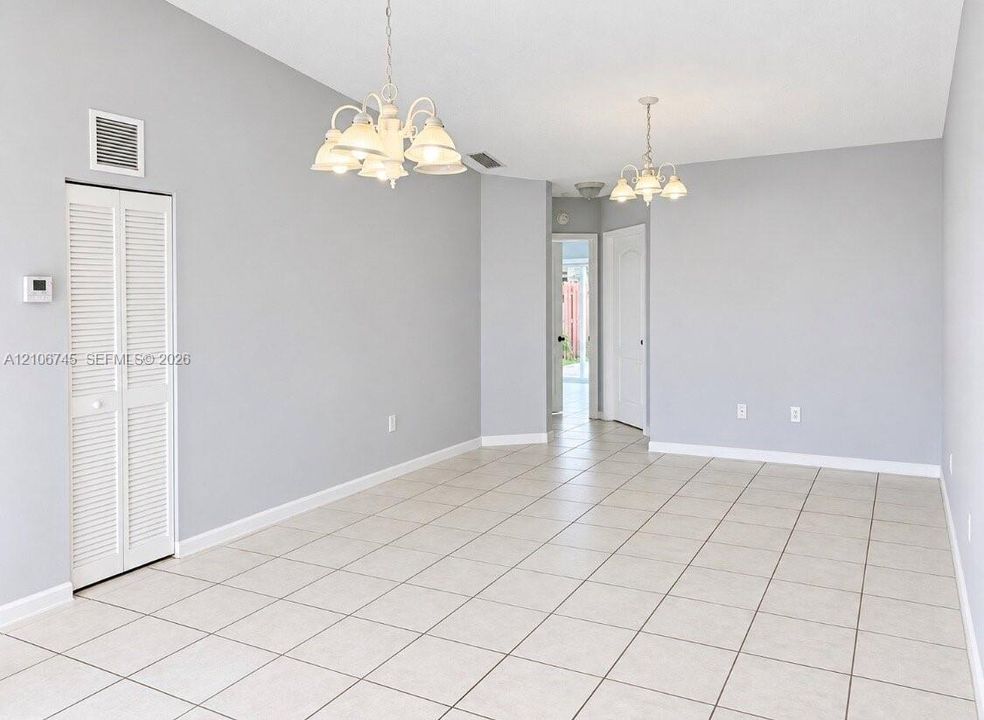 Neutral-toned interior space featuring light-colored tile flooring, dual multi-light chandeliers, and a white louvered-panel closet door