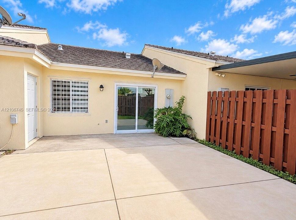 Concrete patio featuring a sliding glass door, exterior wall-mounted lighting, and a wood privacy fence