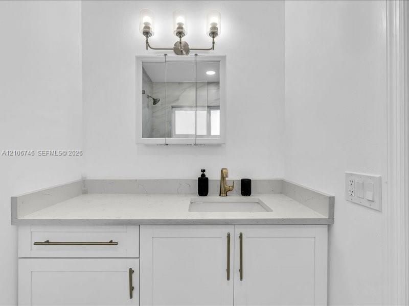 White vanity featuring a solid surface countertop with an integrated basin, brushed metallic faucet, shaker-style cabinetry with elongated hardware, a triple-light wall fixture, and a mirrored medicine cabinet