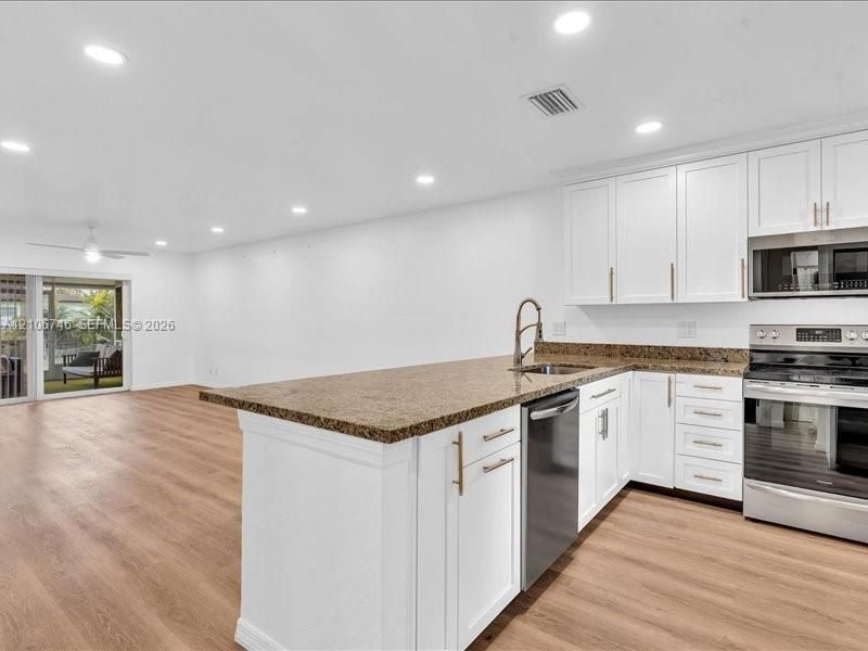 Kitchen featuring white cabinetry with metallic pulls, stone-composite countertops, stainless steel appliances, recessed lighting, and wood-finish flooring