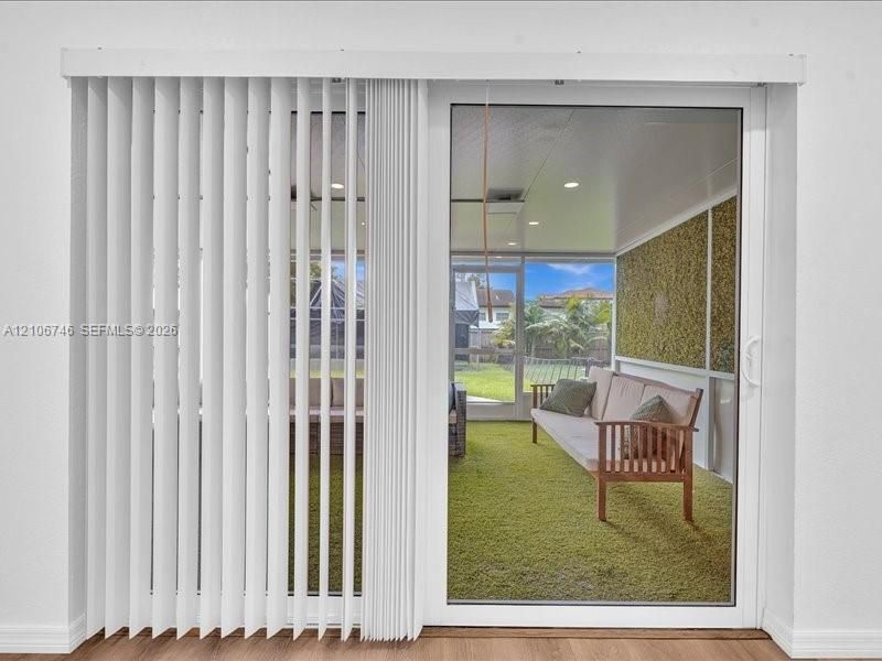 Sliding glass door featuring white vertical blinds, opening to an enclosed porch with recessed ceiling lighting and a textured green accent wall