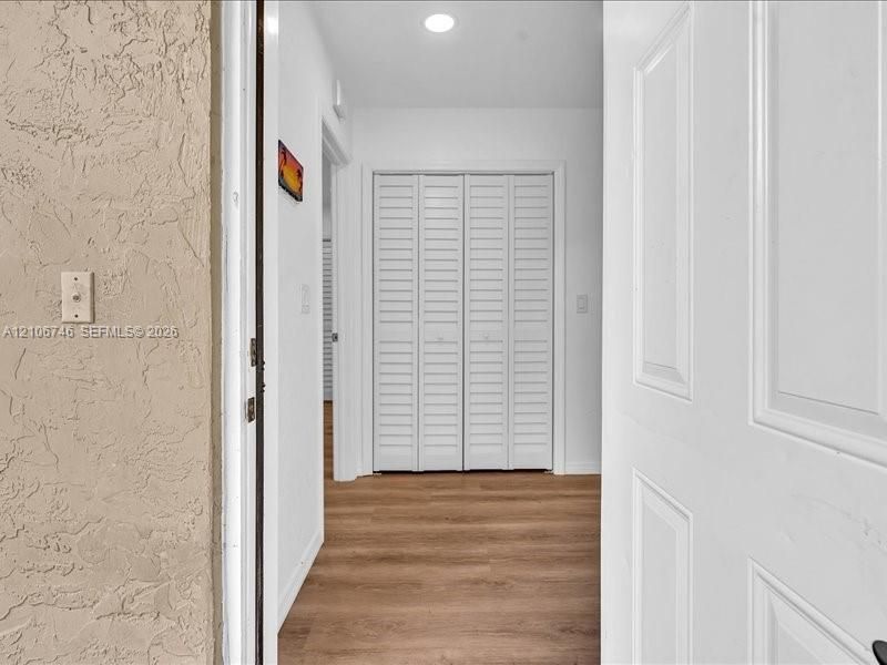Entryway featuring wood-finish flooring, white paneled doors, and louvered closet doors with recessed ceiling lighting
