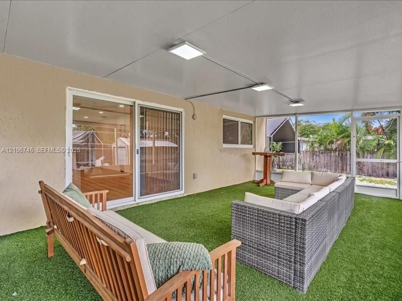 Screened lanai featuring synthetic grass flooring, a solid panel ceiling, surface-mounted square lighting, and dual sliding glass doors