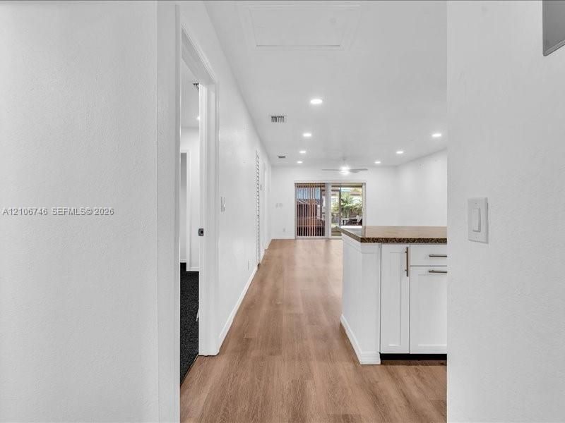 Open interior featuring wood-finish flooring, recessed lighting, white cabinetry with metal hardware, and sliding glass patio doors
