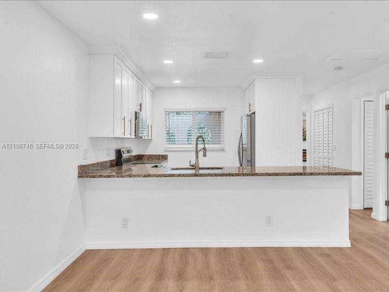 Kitchen featuring white shaker-style cabinetry, stone countertops, stainless steel appliances, a pull-down faucet, and wood-finish flooring