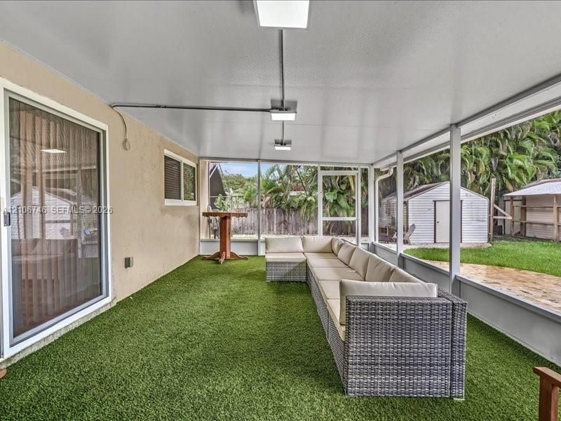 Screened-in patio featuring an artificial turf floor, a covered ceiling with integrated lighting, and access to a backyard area