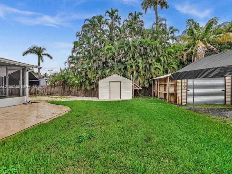Spacious backyard featuring a concrete patio, detached storage shed, metal-roofed structure, and perimeter fencing