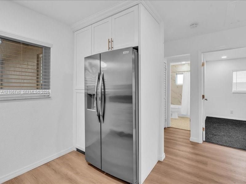 Built-in cabinetry with white finish, stainless steel side-by-side refrigerator, and wood-finish flooring