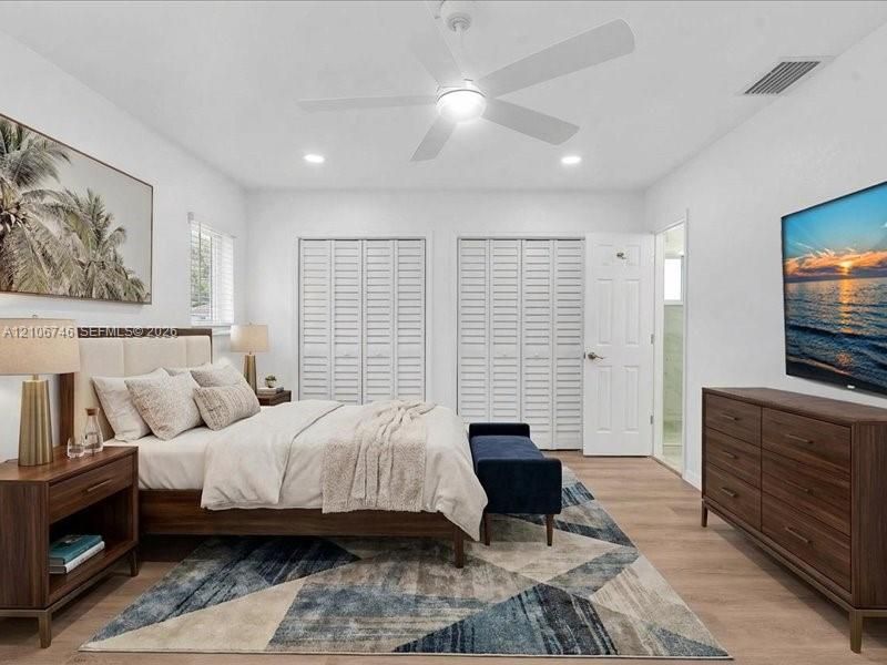 Bedroom featuring wood-finish flooring, dual bi-fold louvered closets, and a white ceiling fan with integrated lighting